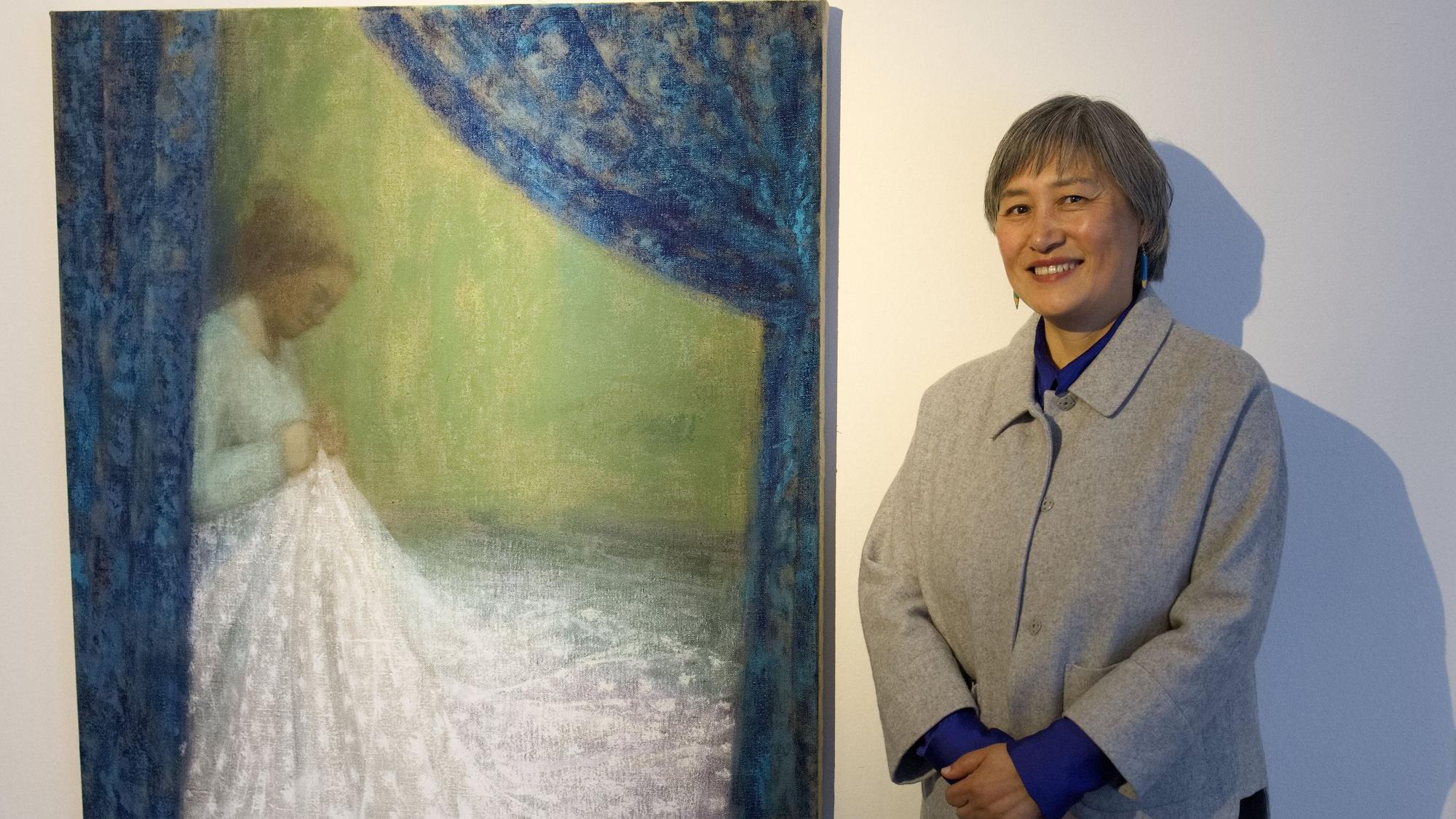 Die Künstlerin vor ihrem Bild, auf dem eine Frau an einem weißen Kleid näht.