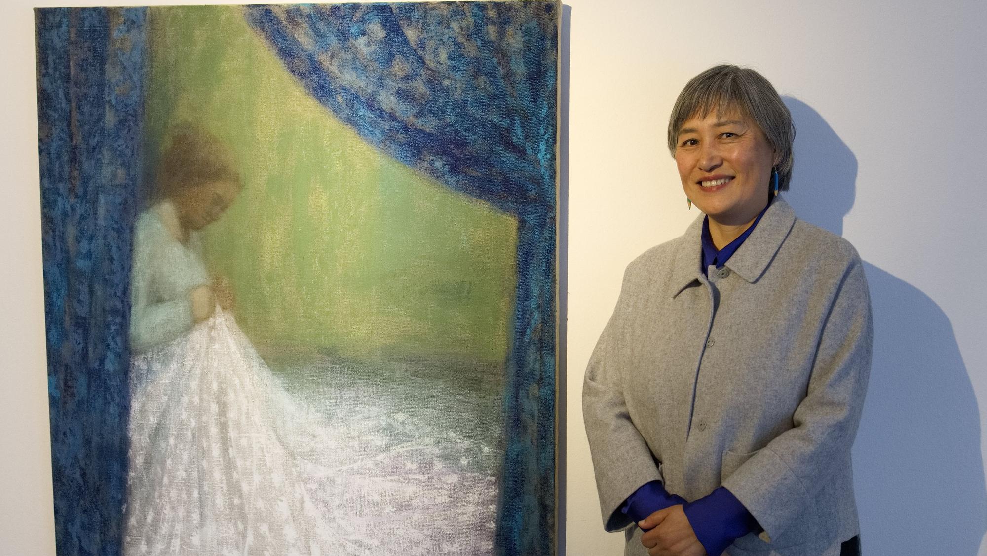 Die Künstlerin vor ihrem Bild, auf dem eine Frau an einem weißen Kleid näht.