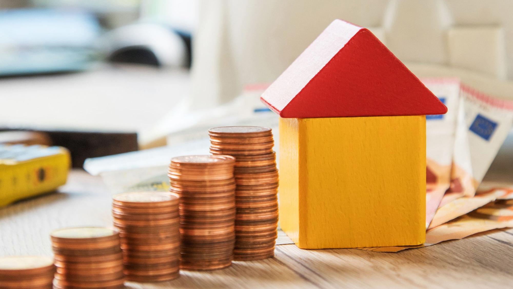 Münzen und ein Haus aus Bausteinen liegen auf einem Tisch