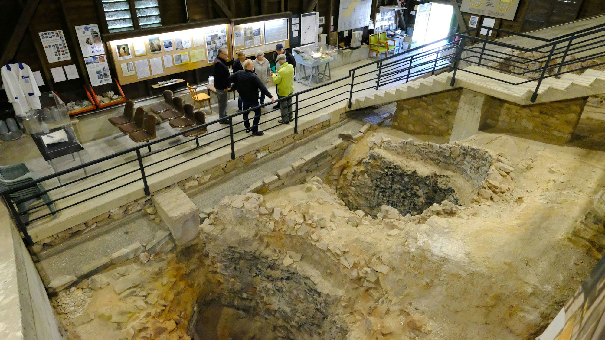 Besucher in der römischen Kalkbrennerei in Iversheim nehmenan einer Führung teil. Im Vordergrund sind die Überreste von zwei römischen Kalköfen zu sehen.