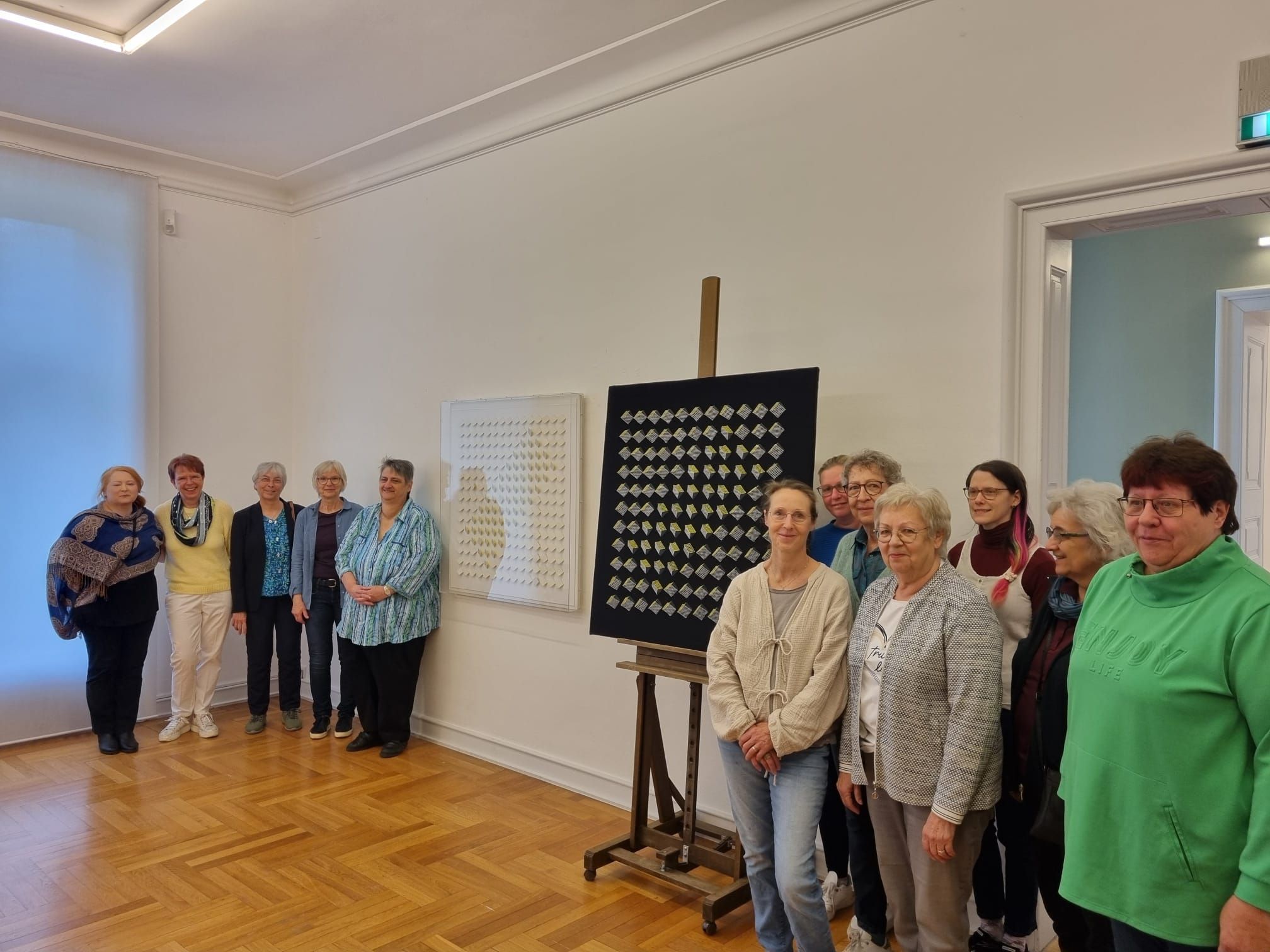 Frauen stehen in einem Raum um ein geklöppeltes Kunstwerk.