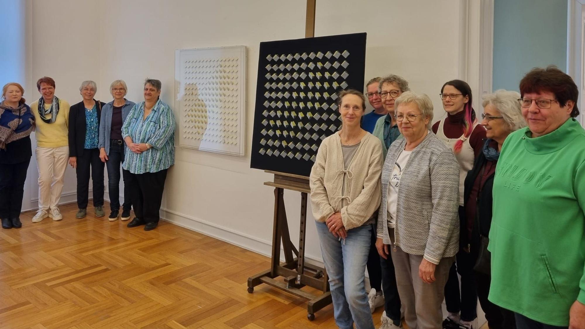 Frauen stehen in einem Raum um ein geklöppeltes Kunstwerk.