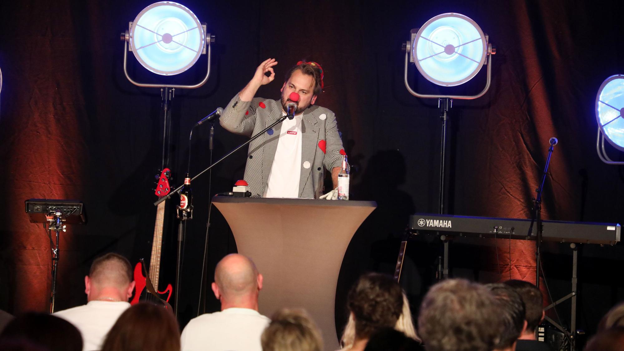 Ein Mann steht als Büttenredner mit Pappnase auf einer Bühne.