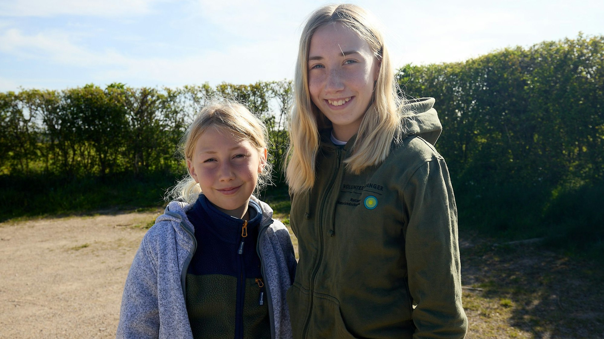Beide Geschwister haben blonde Haare und schauen lächelnd in die Kamera.