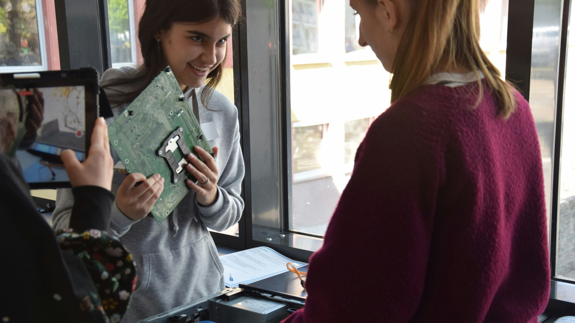 Eine Schülerin hält das grüne Motherboard eines Computers in der Hand.