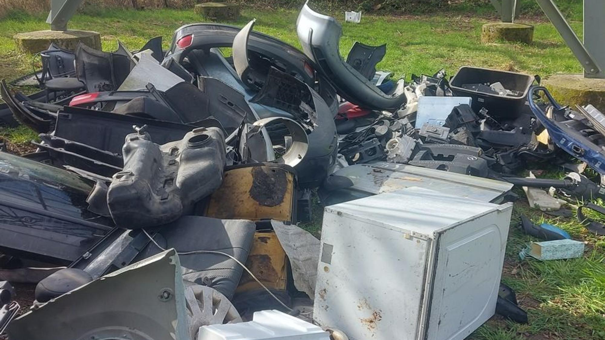 Ein Haufen illegal entsorgter Müll mit Autoteilen liegt in der Natur.