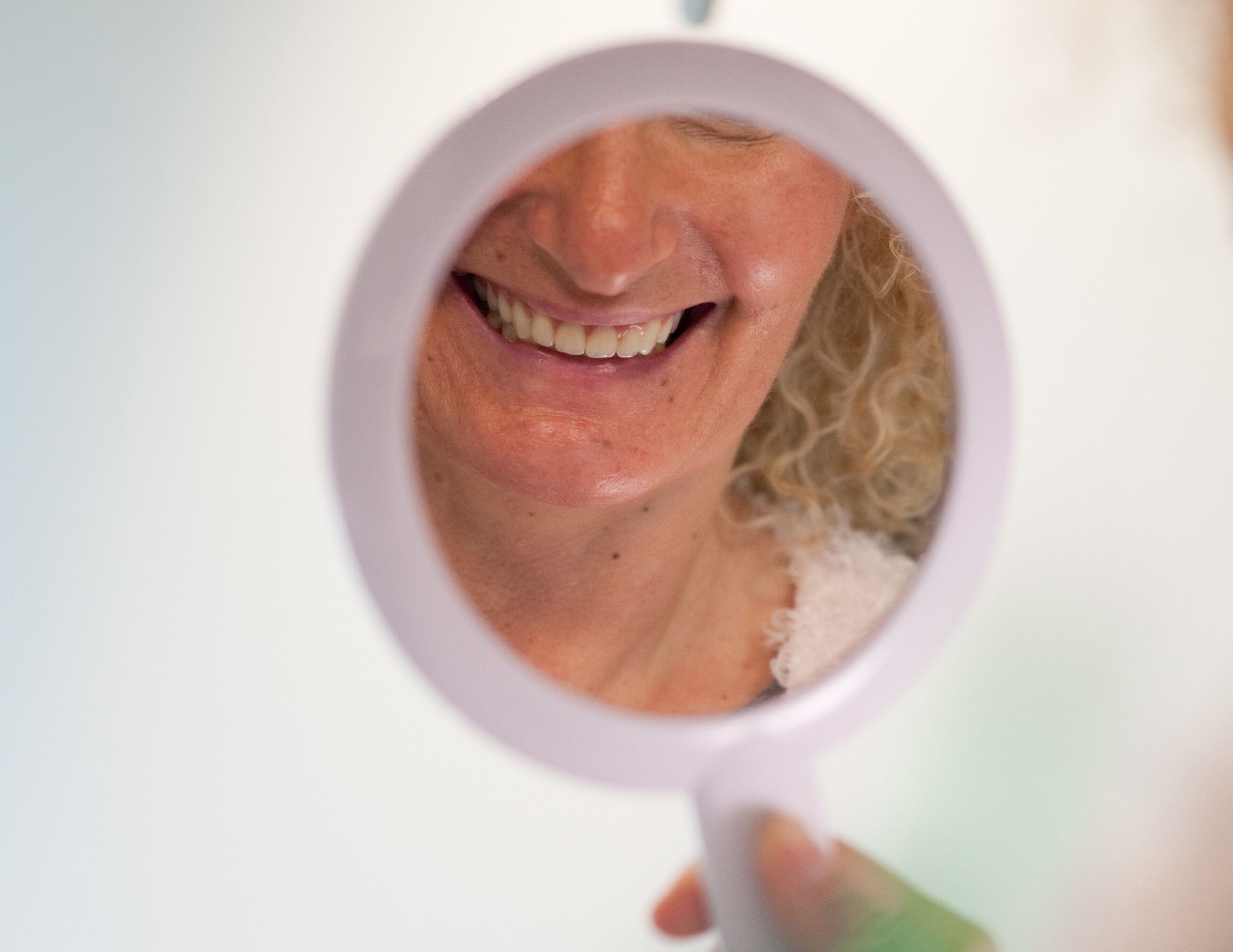 Frau schaut sich ihre Zähne in einem Handspiegel an