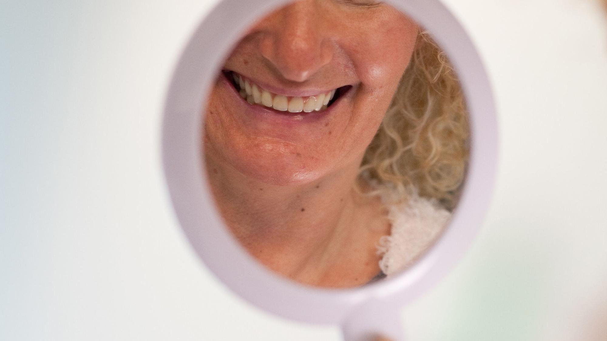 Frau schaut sich ihre Zähne in einem Handspiegel an