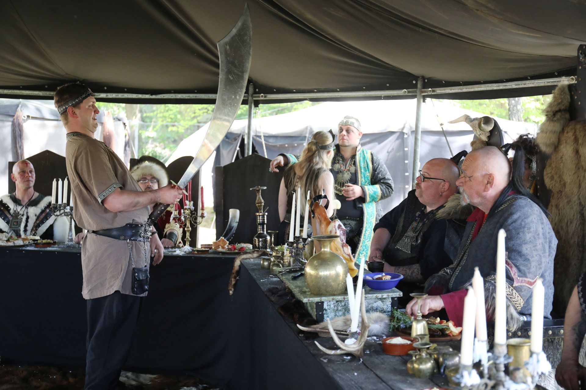 Eine Gruppe von Menschen, die als Hunnen verkleidet sind, an einer Tafel. Einer hebt ein schweres Schwert.