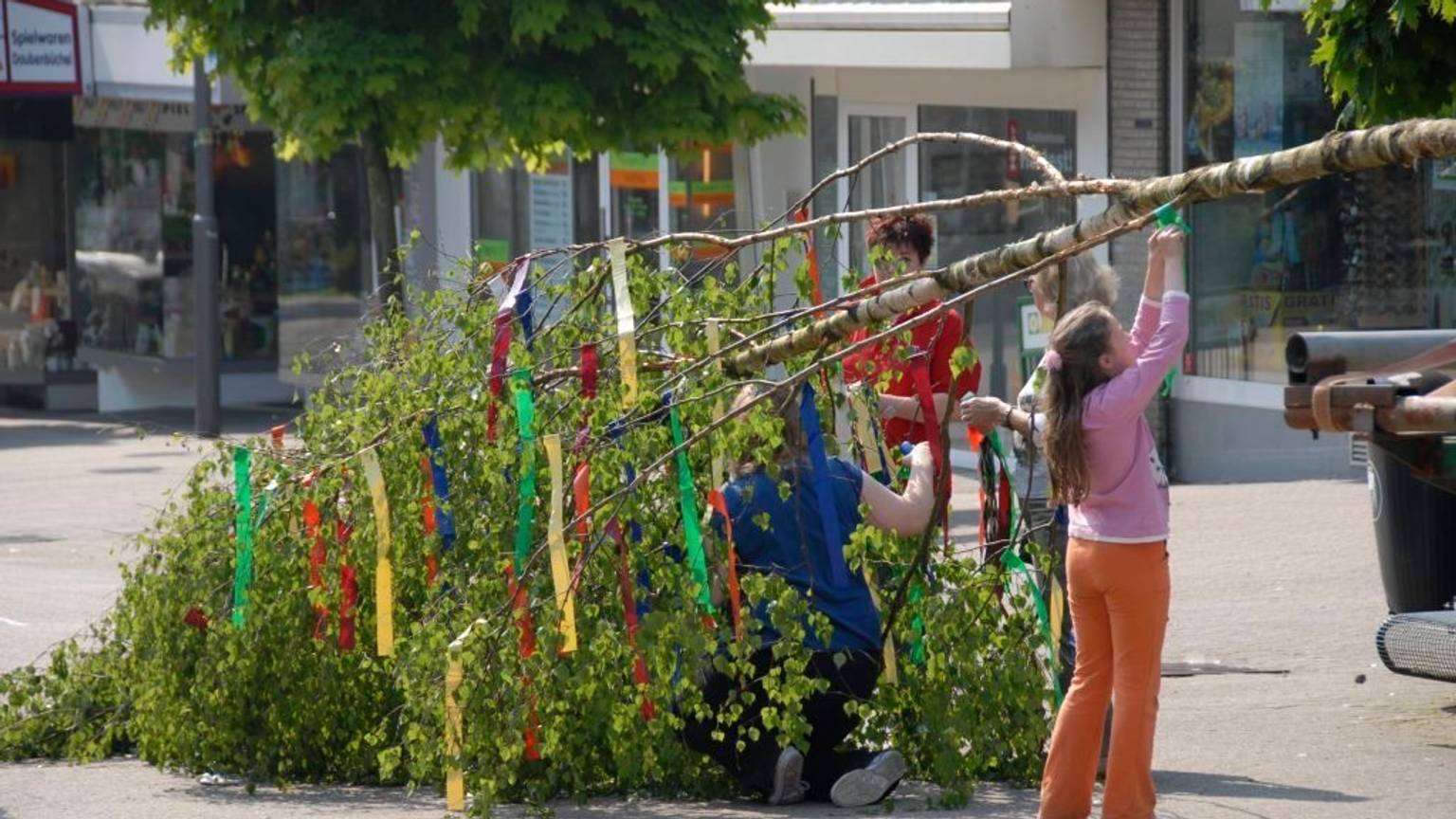 Kinder helfen einen Maibaum zu schmücken.