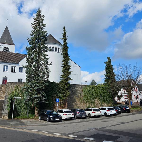 Blick auf die Kirche und die Mauer unterhalb, an der mehrere Autos parken.