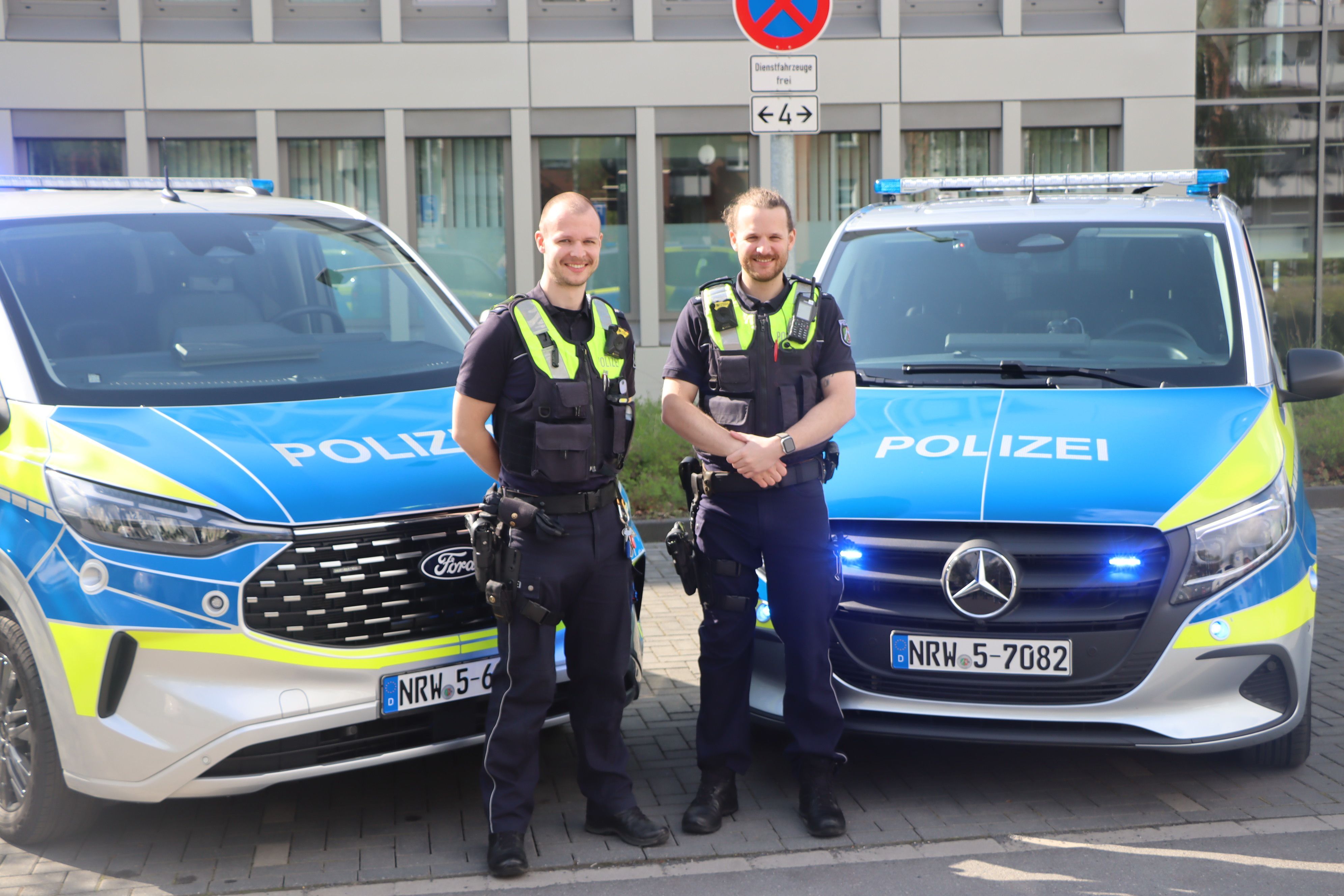 Zwei Polizisten stehen vor zwei Streifenwagen.