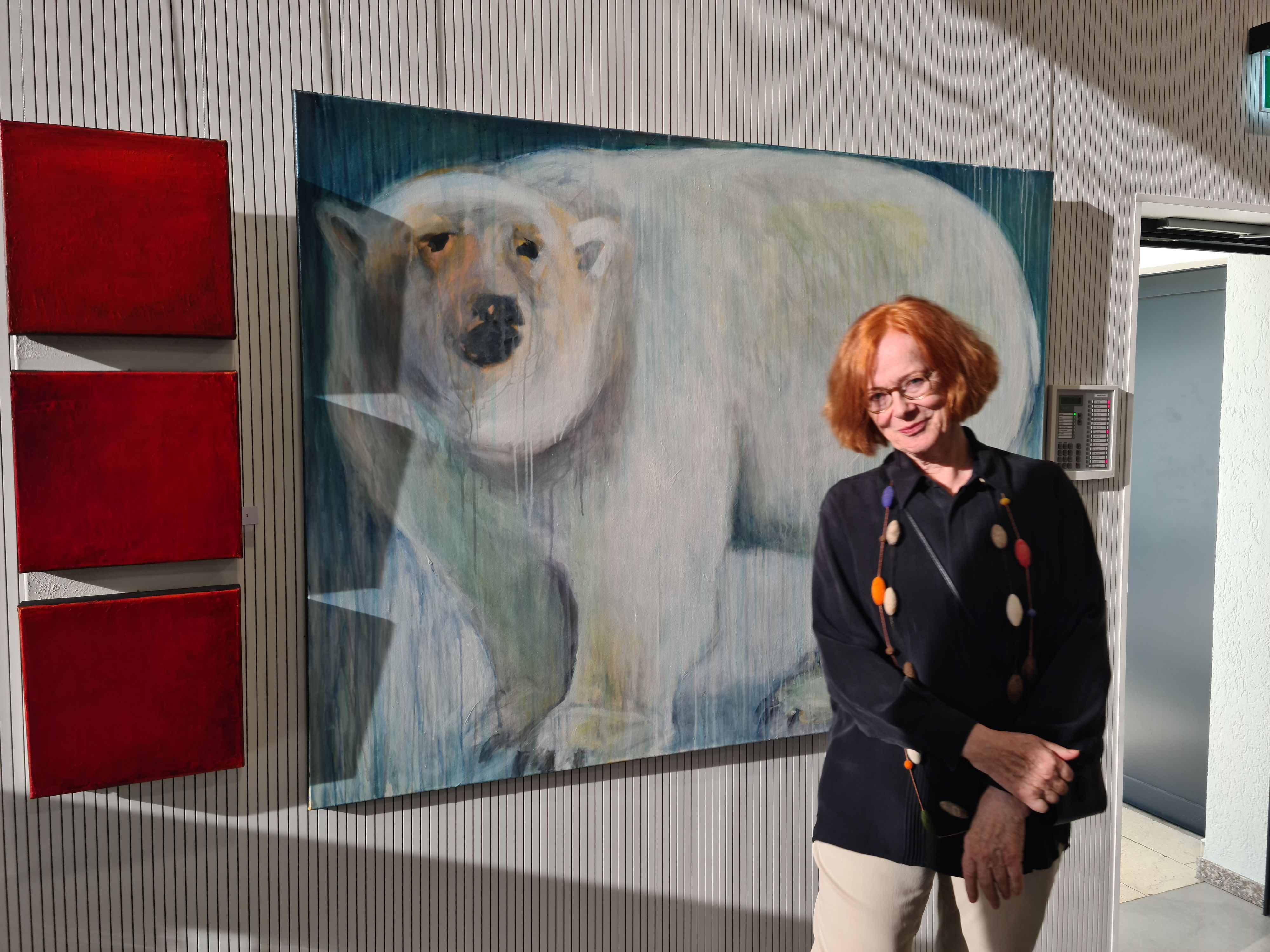 Eine Frau mit rotem Haar steht vor dem großformatigen Bild eines Eisbären.