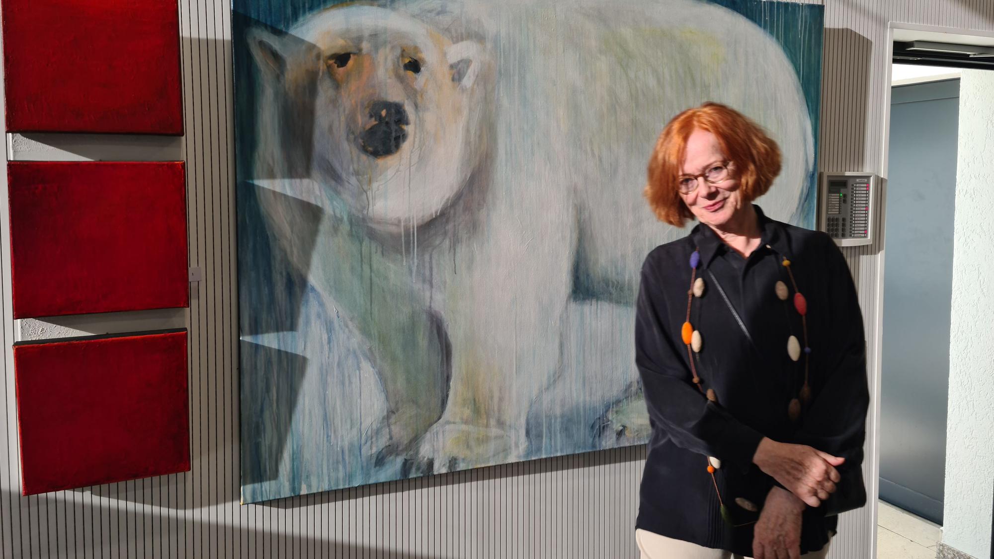 Eine Frau mit rotem Haar steht vor dem großformatigen Bild eines Eisbären.