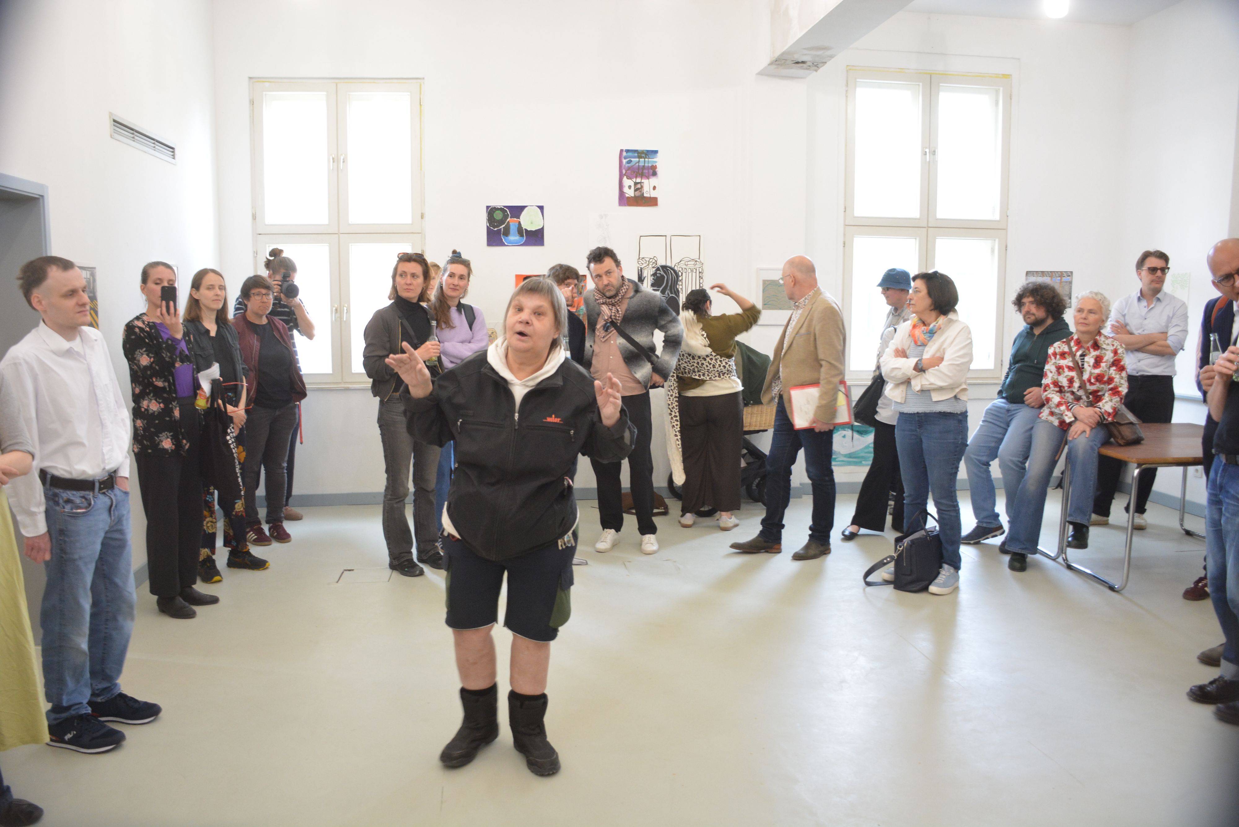Eine Frau steht gestkulierend in einem Raum und spricht zu Menschen.
