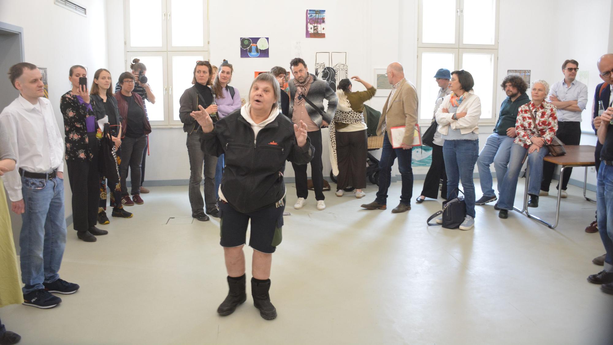 Eine Frau steht gestkulierend in einem Raum und spricht zu Menschen.