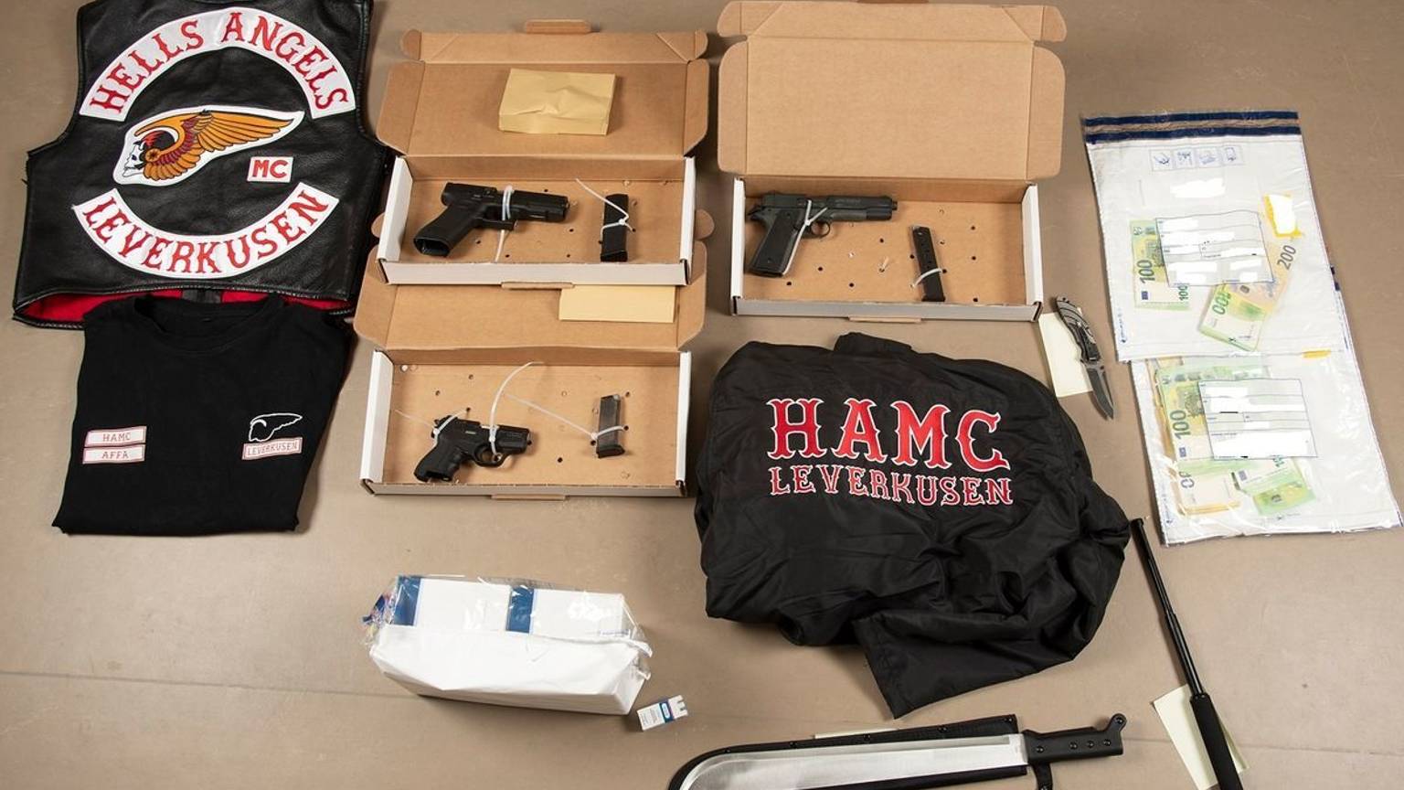 HANDOUT - 28.04.2026, Nordrhein-Westfalen, Düsseldorf: Sichergestellte Gegenstände und Bargeld liegen auf einem Tisch. Bei den Razzien gegen «Hells Angels»-Rocker in Nordrhein-Westfalen haben die Ermittlungsbehörden u.a. Waffen und Vermögenswerte sichergestellt. Foto: Polizei Düsseldorf/