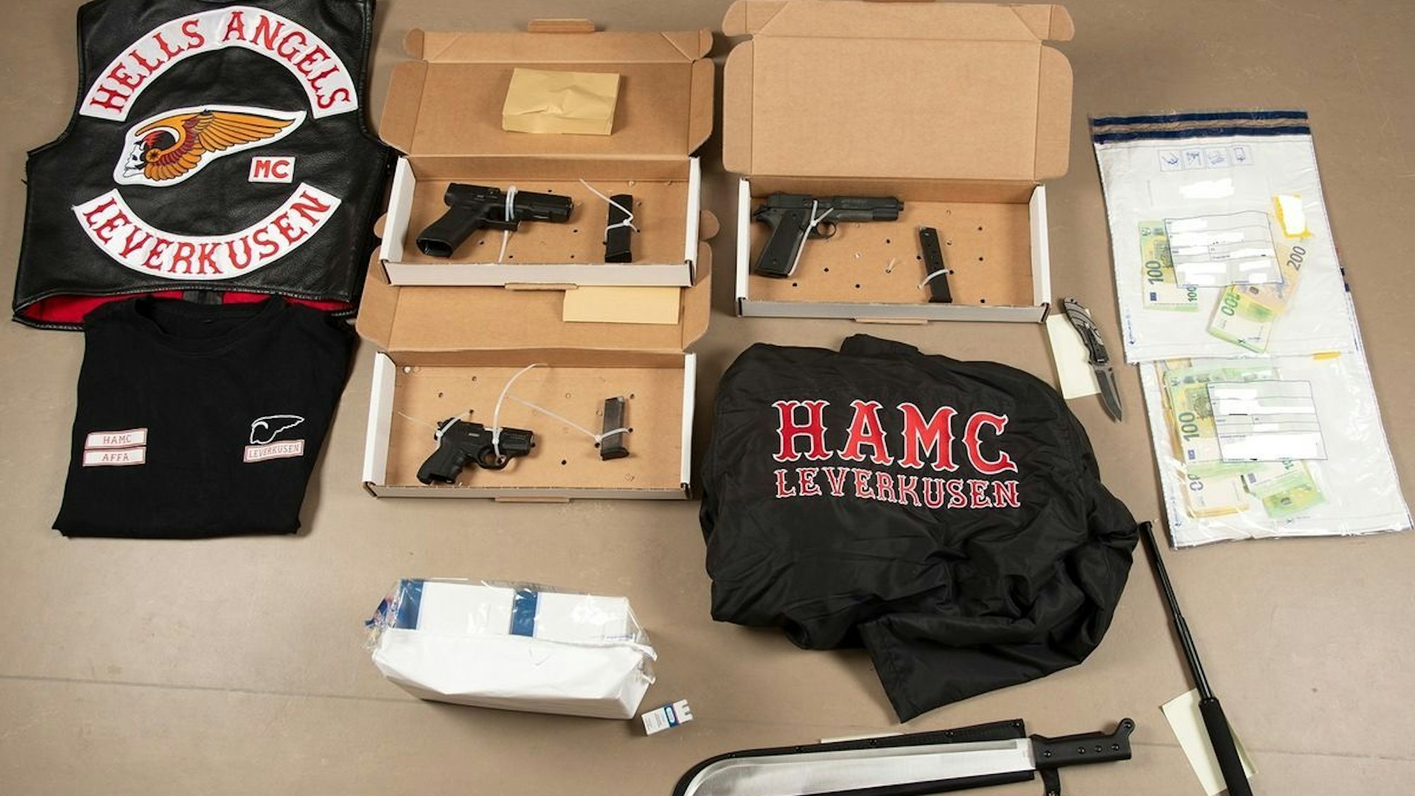 Sichergestellte Gegenstände und Bargeld liegen auf einem Tisch. Bei den Razzien gegen Hells Angels-Rocker in Nordrhein-Westfalen haben die Ermittlungsbehörden unter anderem Waffen und Vermögenswerte sichergestellt.