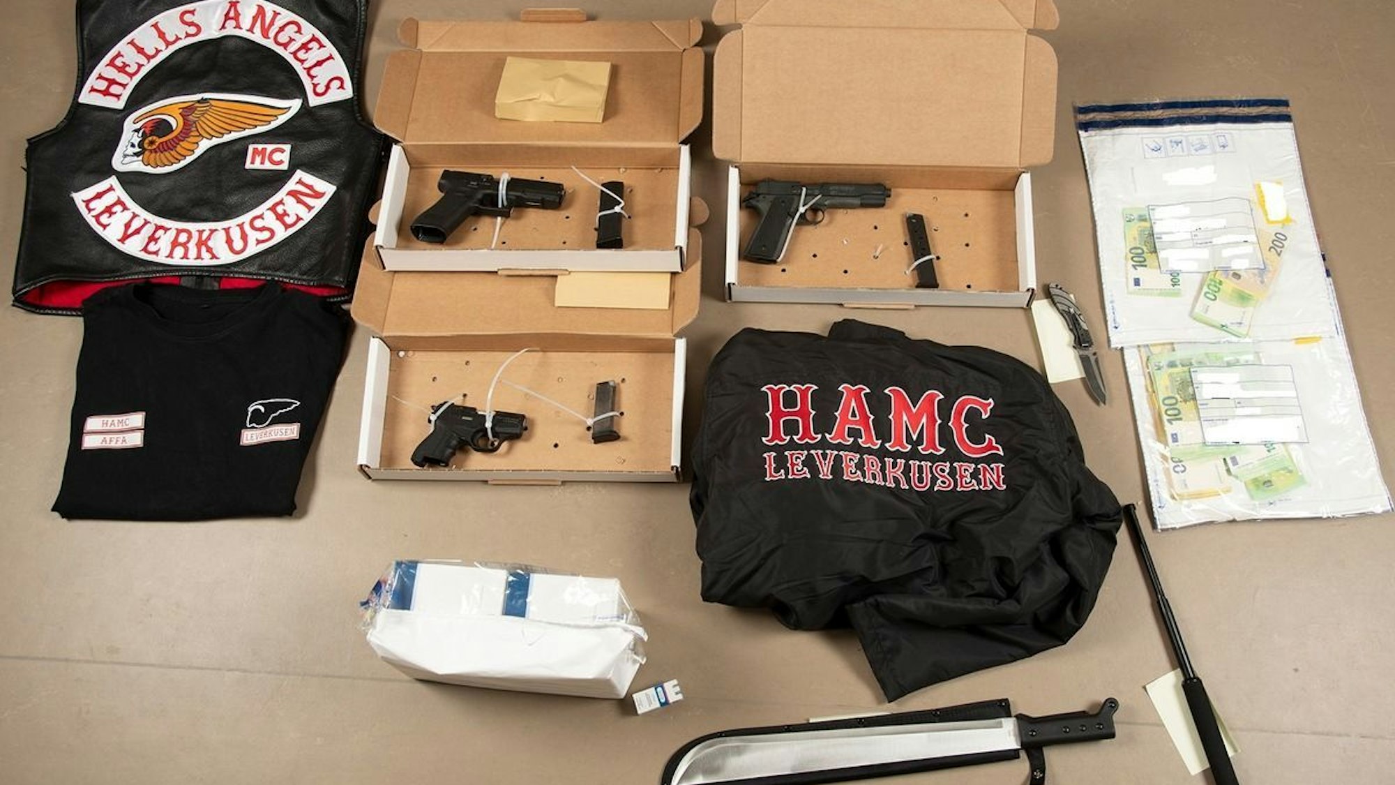 HANDOUT - 28.04.2026, Nordrhein-Westfalen, Düsseldorf: Sichergestellte Gegenstände und Bargeld liegen auf einem Tisch. Bei den Razzien gegen «Hells Angels»-Rocker in Nordrhein-Westfalen haben die Ermittlungsbehörden u.a. Waffen und Vermögenswerte sichergestellt. Foto: Polizei Düsseldorf/