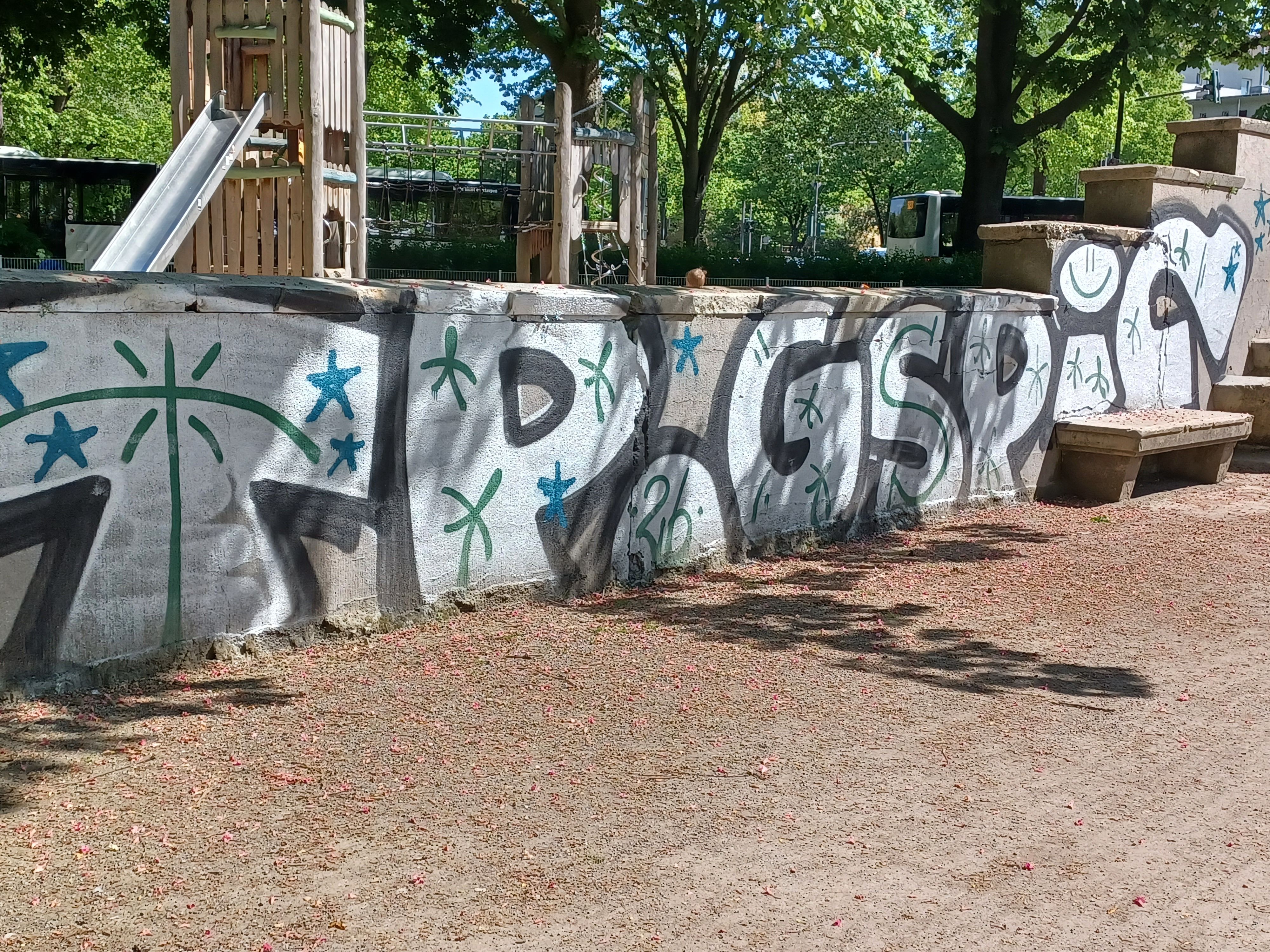 Große Graffiti-Tags ziehen sich an einer Mauer entlang.