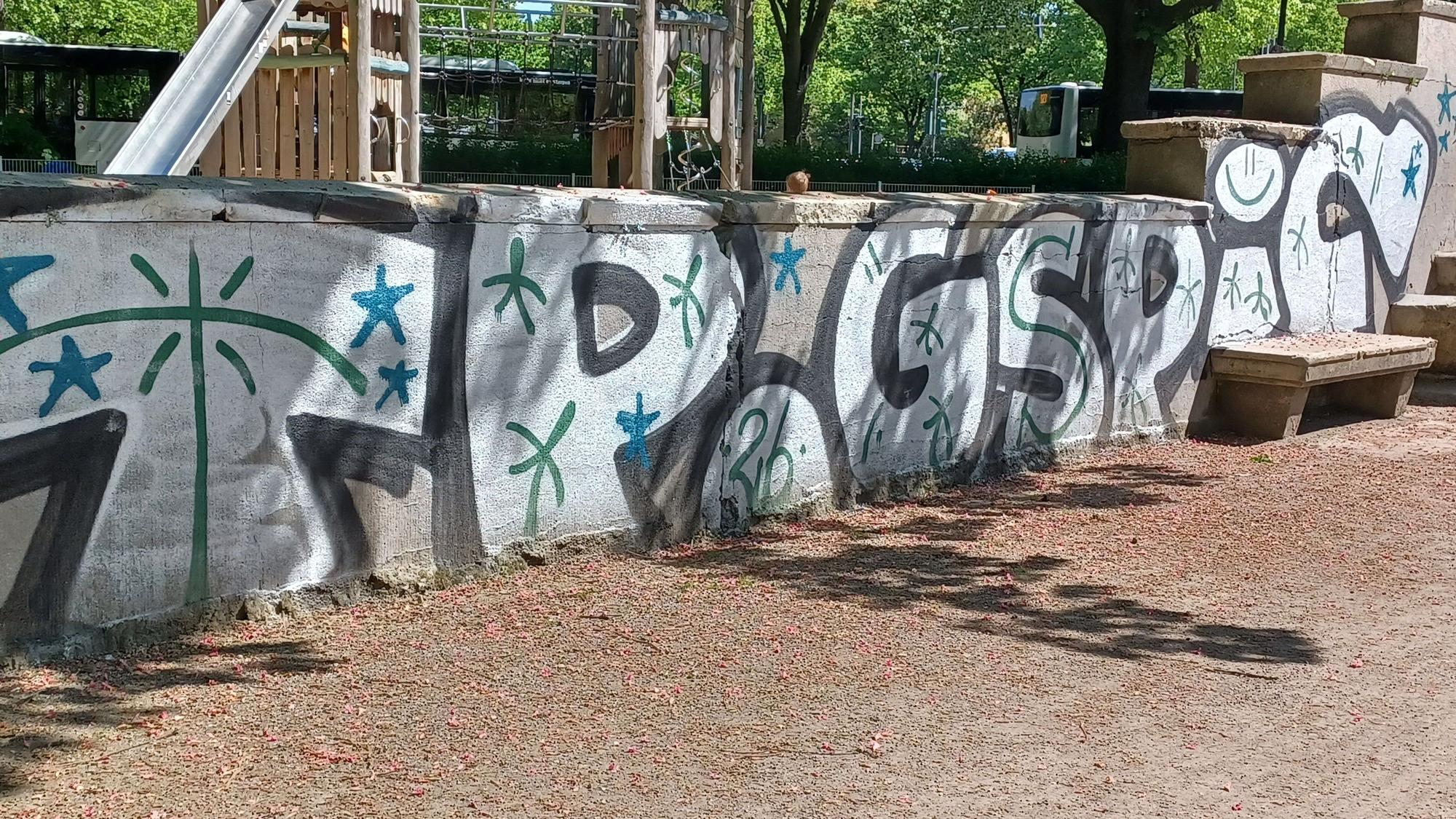 Große Graffiti-Tags ziehen sich an einer Mauer entlang.