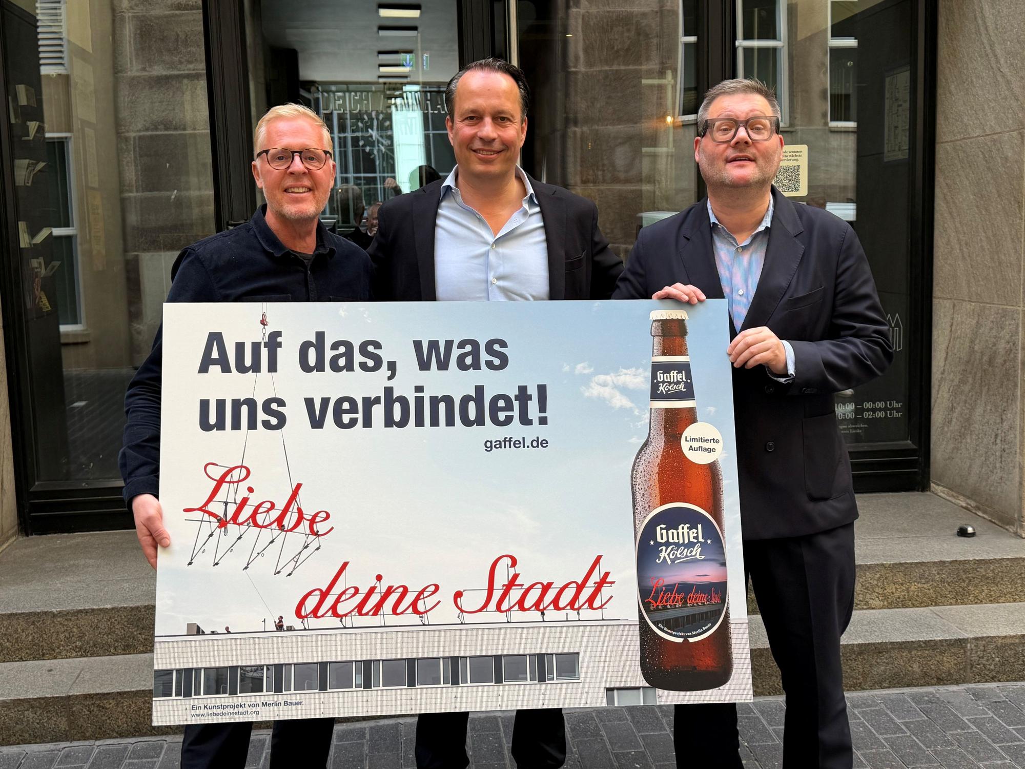 Thomas Deloy, Heinrich Philipp Becker und Künstler Merlin Bauer zeigen ein Poster.
