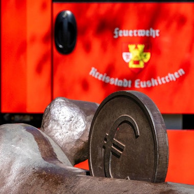 Das Bild zeigt ein Fahrzeug der Euskirchener Feuerwehr. Im Vordergrund ist eine Euro-Münze eines Kunstwerks zu sehen.