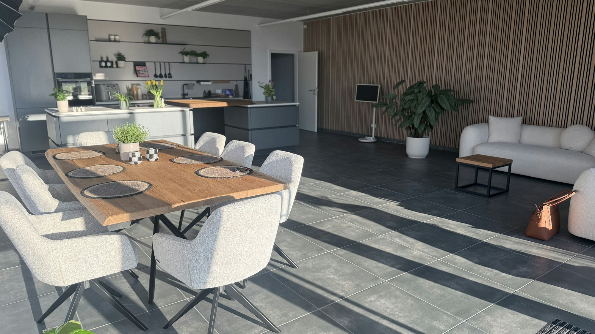 Das Bild zeigt ein Kochstudio mit Küche, Kücheninsel, großem Esstisch und Couch.