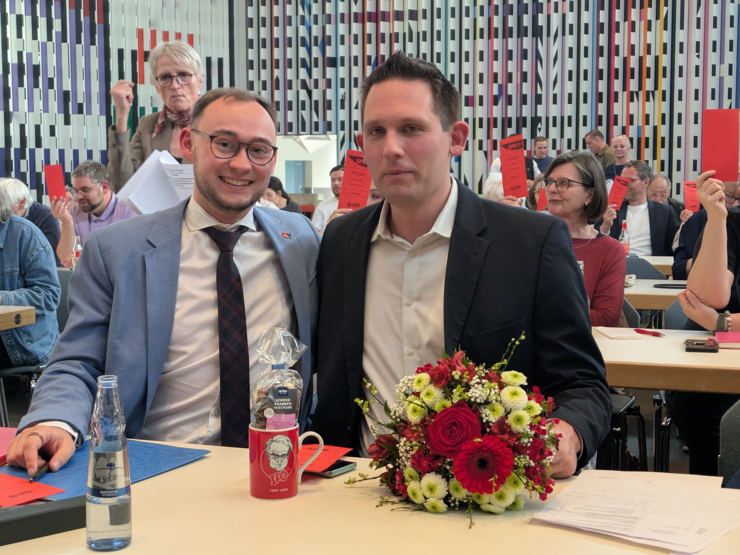 Zwei Männer sitzen an einem Tisch mit Blumen.