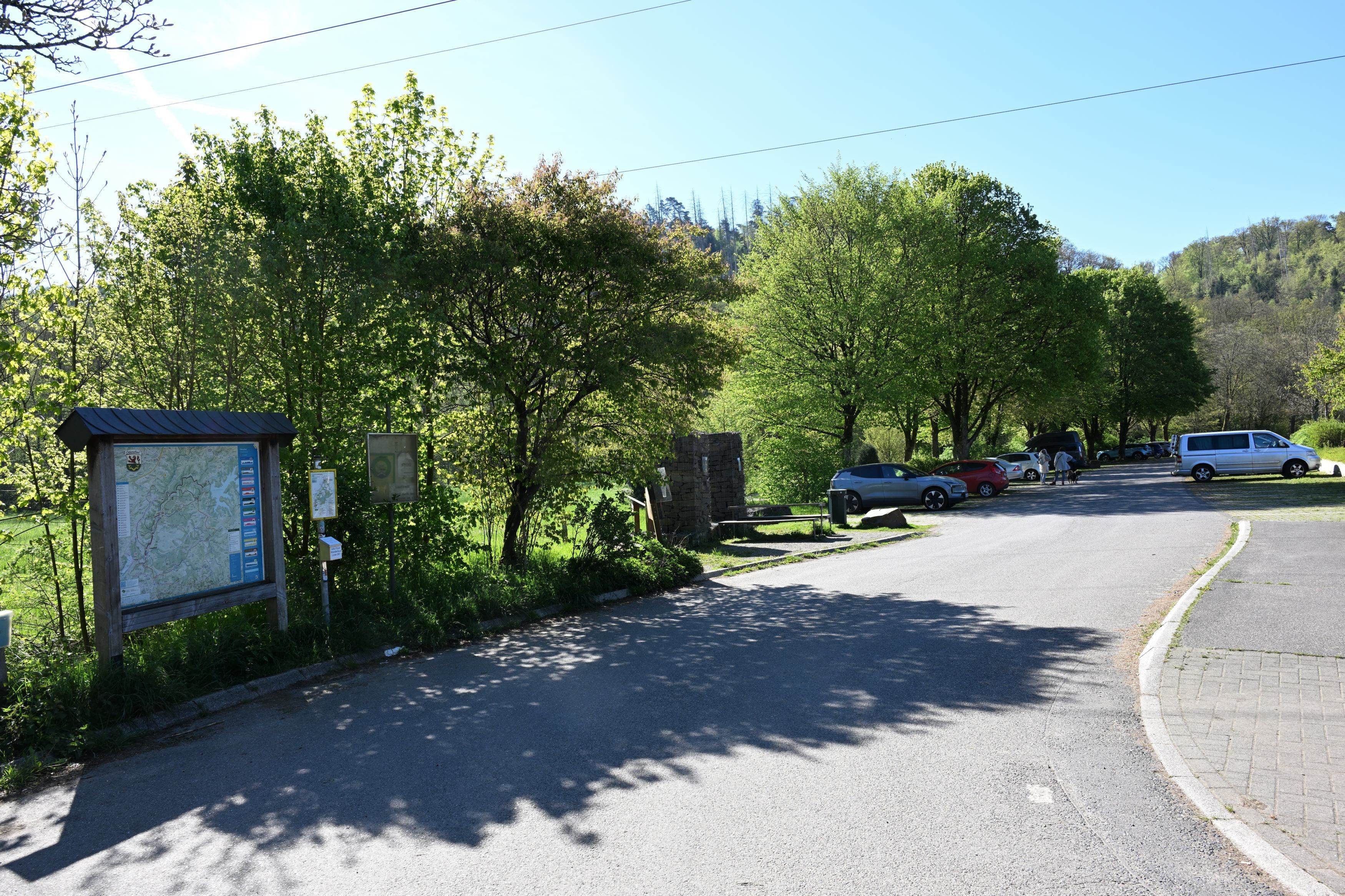 Ein Parkplatz mit einigen Autos im Grünen. An der Zufahrt eine große Wanderkarte.