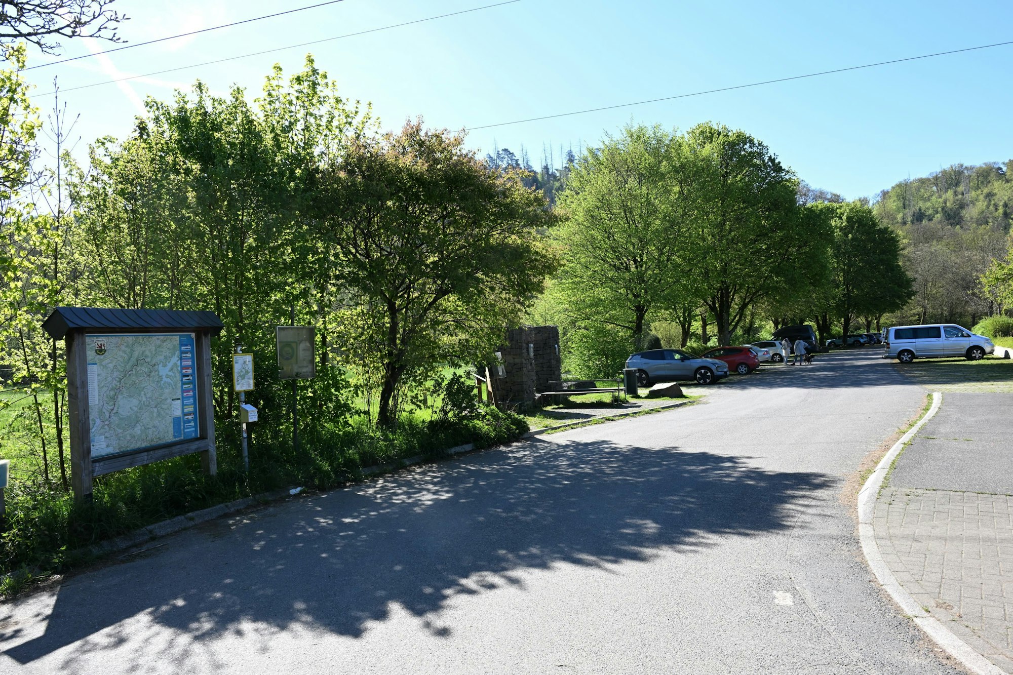 Ein Parkplatz mit einigen Autos im Grünen. An der Zufahrt eine große Wanderkarte.