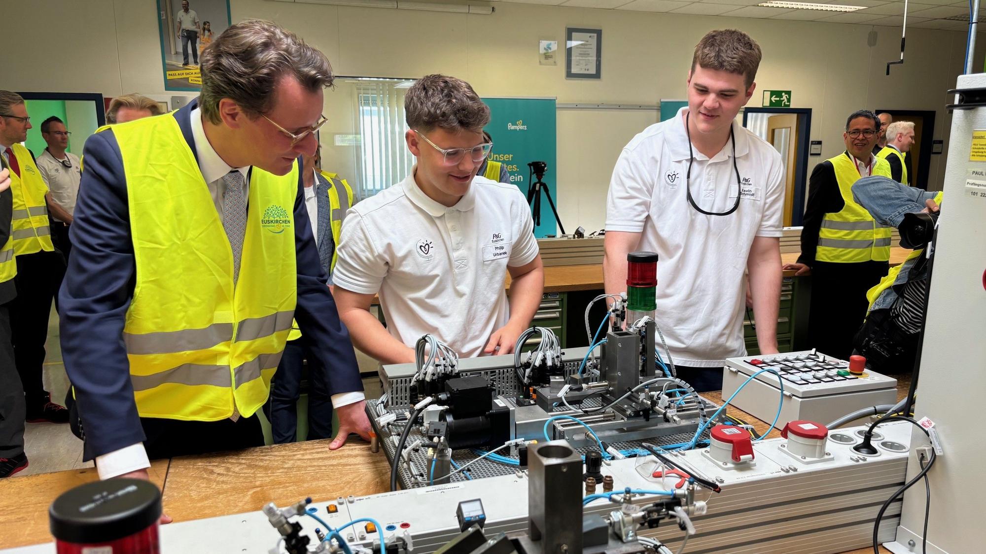 Zwei Auszubildende demonstrieren Hendrik Wüst im Procter & Gamble-Werk Euskirchen technisches Equipment.
