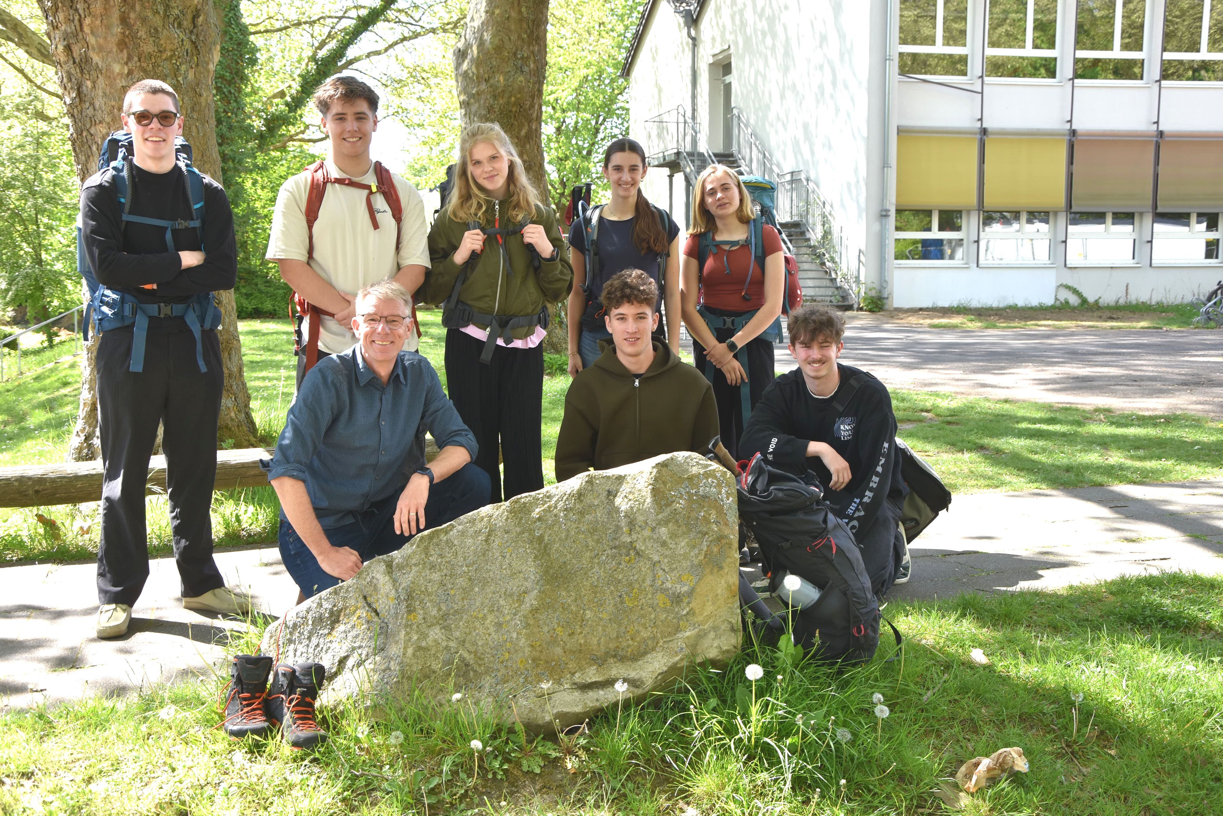 Schüler stehen und knien um einen großen Stein herum auf einem Schulgelände.