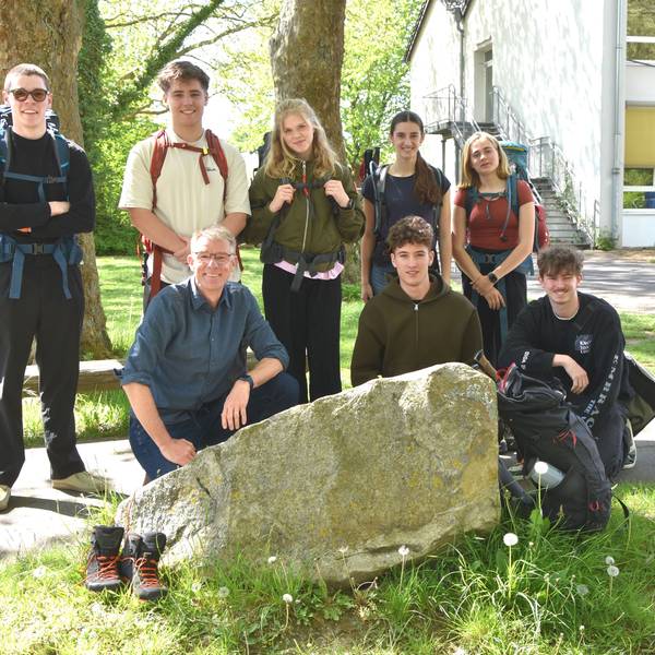 Schüler stehen und knien um einen großen Stein herum auf einem Schulgelände.