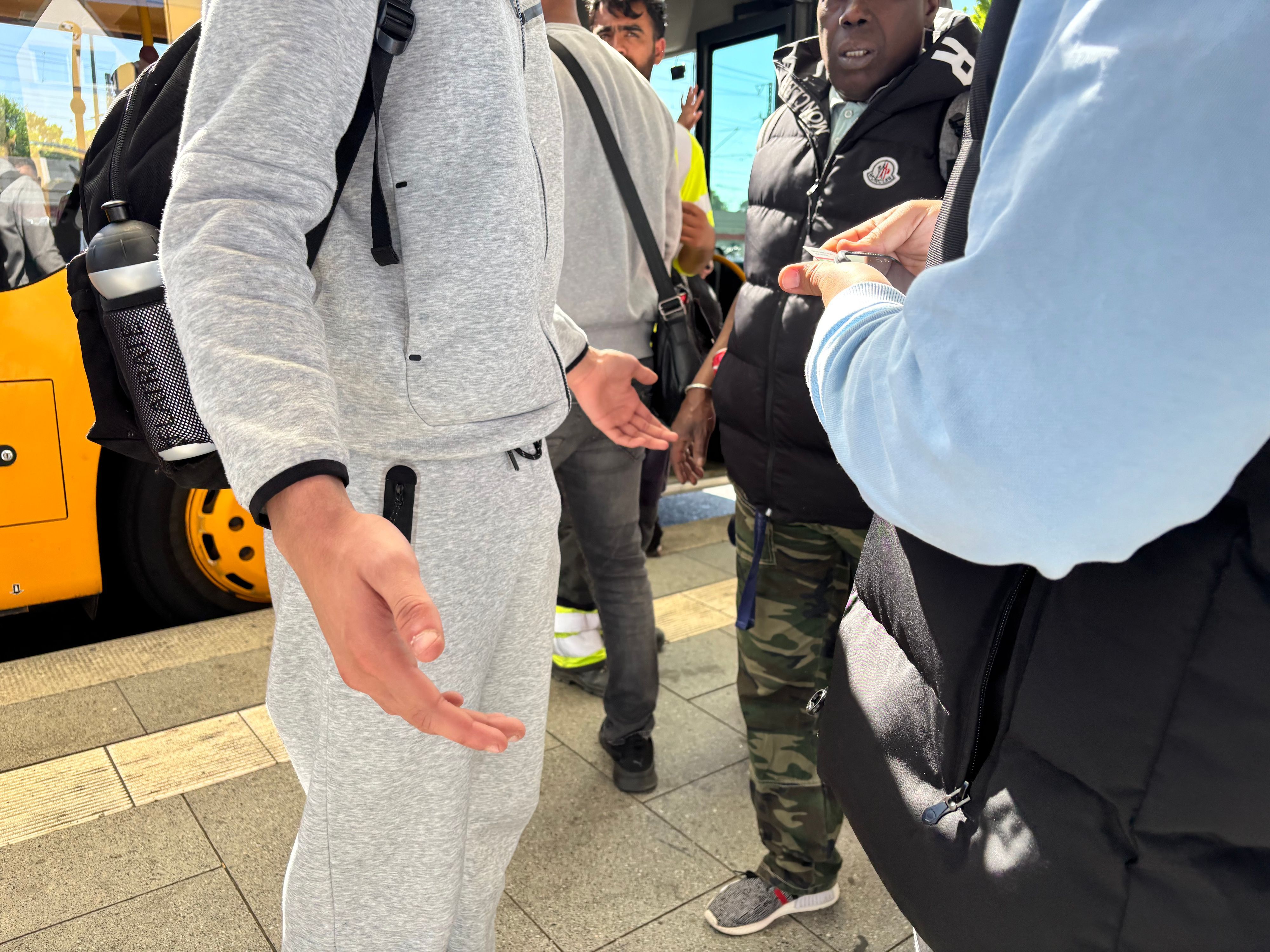Eine Person in einem grauen Trainingsanzug macht eine ausladende Geste mit beiden Händen, während ein Kontrolleuer vor ihr steht. Die Gesichter der Beteiligten sind abgeschnitten.