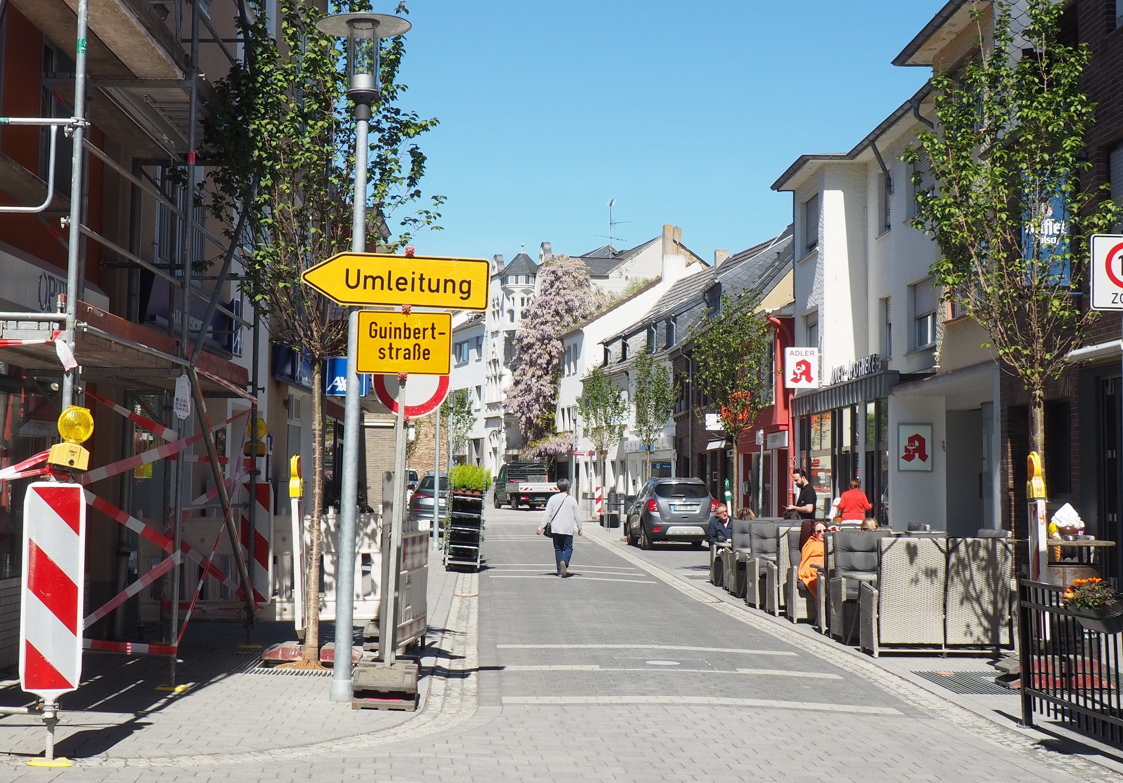 Ein Blick auf die Münsterstraße. Links stehen Baugerüste und ein Umleitungsschild, rechts sitzen Menschen in einem Straßencafé.