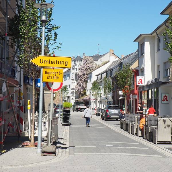 Ein Blick auf die Münsterstraße. Links stehen Baugerüste und ein Umleitungsschild, rechts sitzen Menschen in einem Straßencafé.