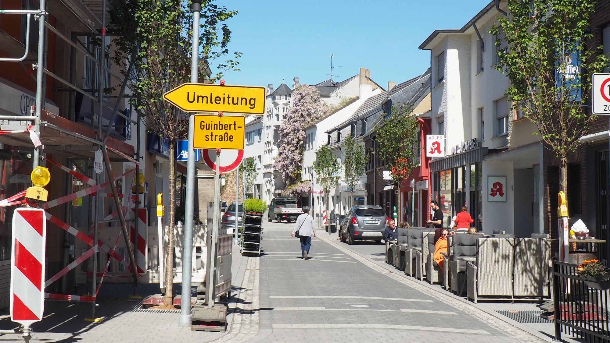 Ein Blick auf die Münsterstraße. Links stehen Baugerüste und ein Umleitungsschild, rechts sitzen Menschen in einem Straßencafé.