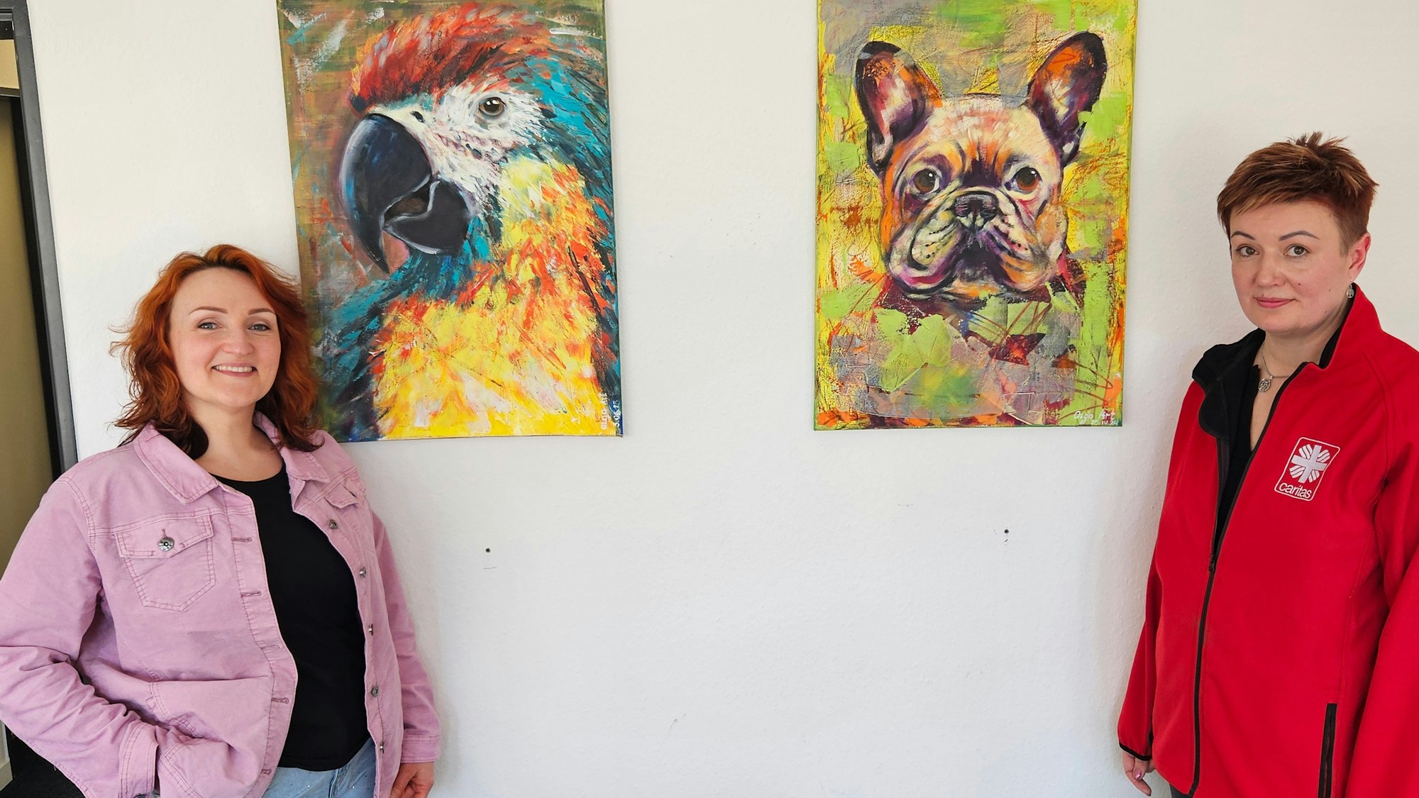 Die beiden Frauen stehen vor einer Wand, an der zwei Tierbilder hängen.