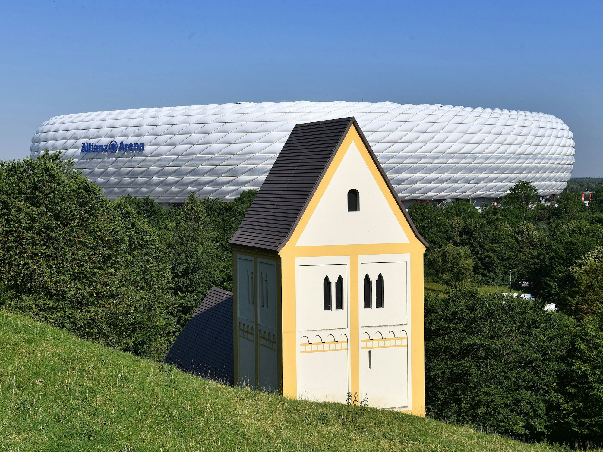 Die Nachbildung einer Kirche steht halb im Boden versunken vor einem Fußballstadion.
