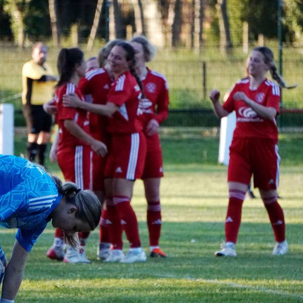 Im Hintergrund jubelt eine Fußballmannschaft, im Vordergrund beugt sich die gegnerische Torhüterin nach vorne