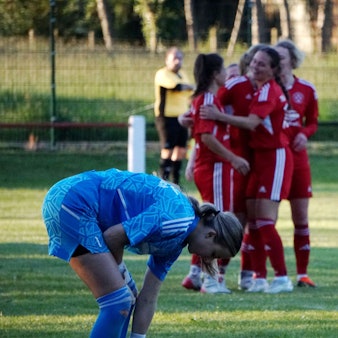 Im Hintergrund jubelt eine Fußballmannschaft, im Vordergrund beugt sich die gegnerische Torhüterin nach vorne