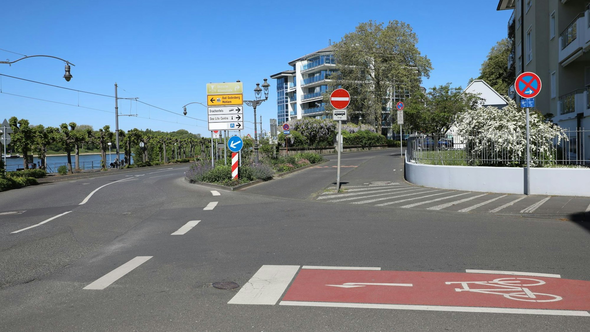 Eine Straßenkreuzung mit einer kurzen Extraspur für Busse, links im Hintergrund die Promenade am Rhein.