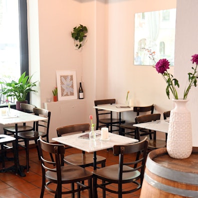 Der Gastraum der Bar mit kleinen Marmor-Tischen und Blumengesteck auf einem Weinfass.