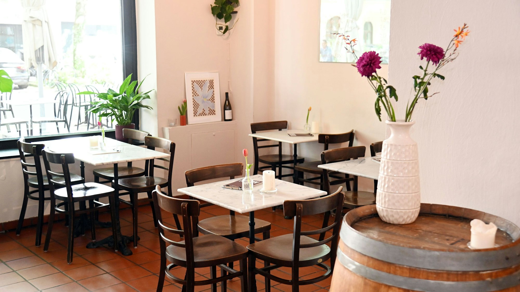 Der Gastraum der Bar mit kleinen Marmor-Tischen und Blumengesteck auf einem Weinfass.
