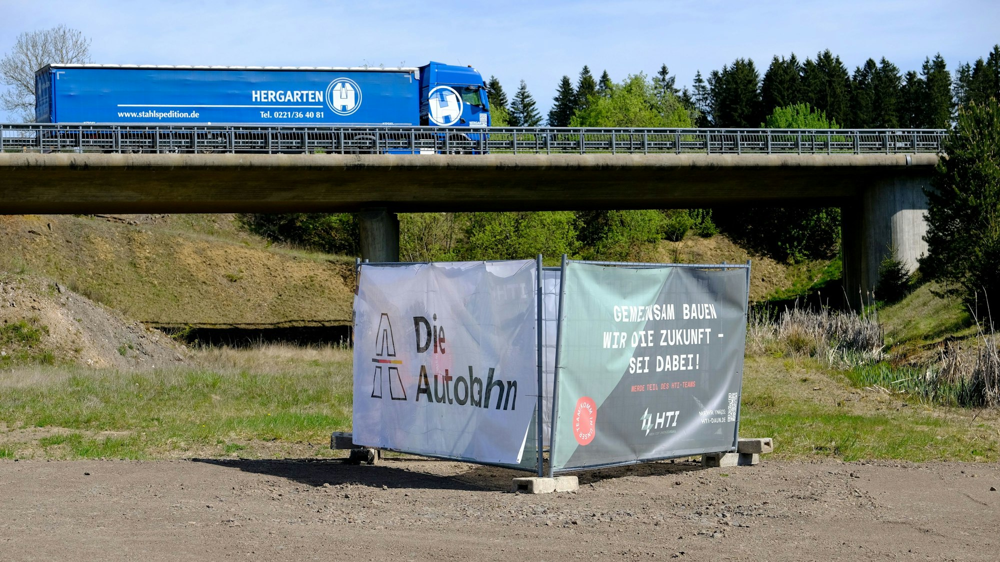 Beim Autobahnende der A1 in Rheinland-Pfalz fährt ein blauer LKW über eine Brücke, die über die künftige Autobahntrasse führt.