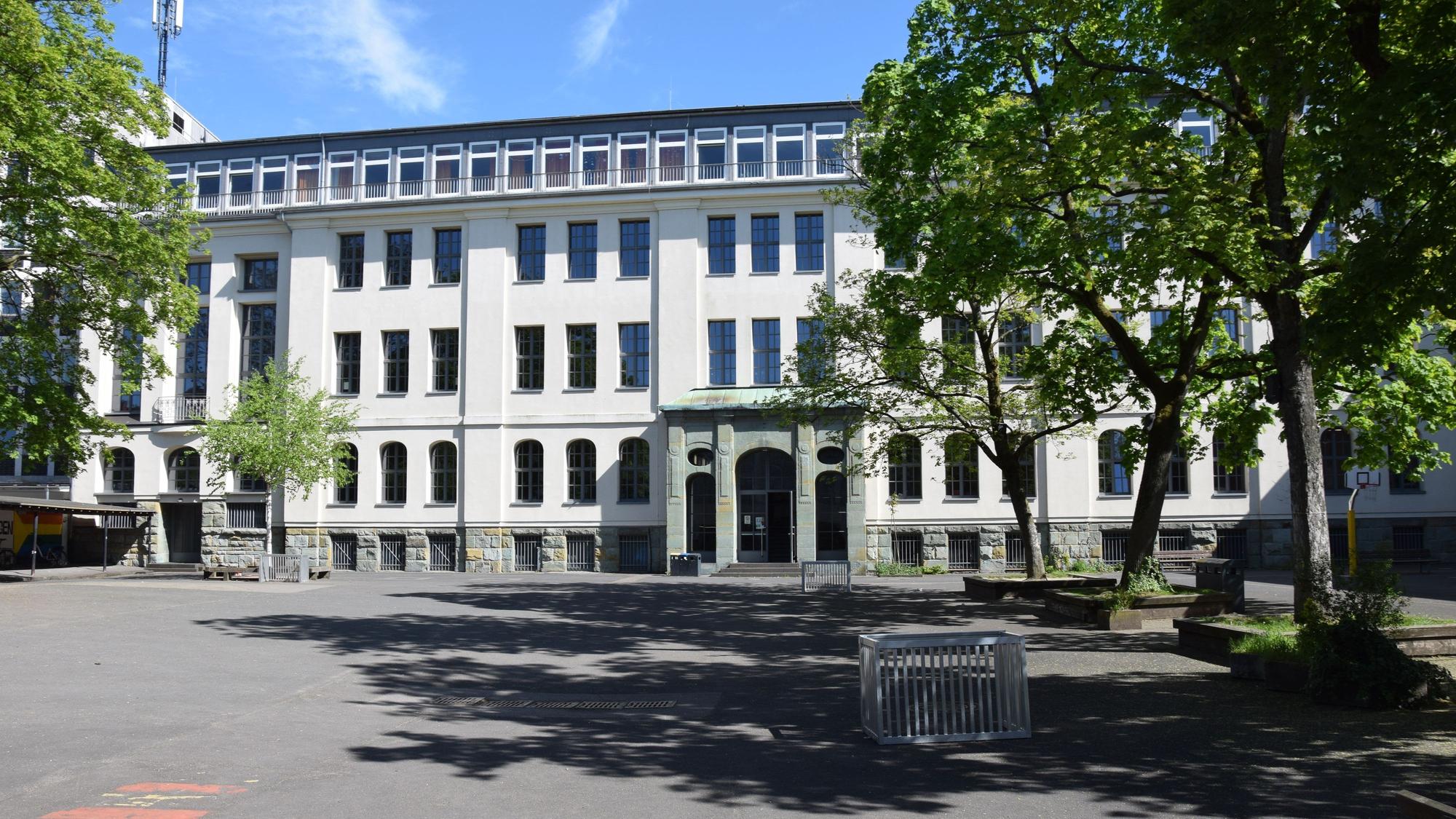 Hinter einem Schulhof steht ein mehrtöckiges weiß getünchtes Gebäude.