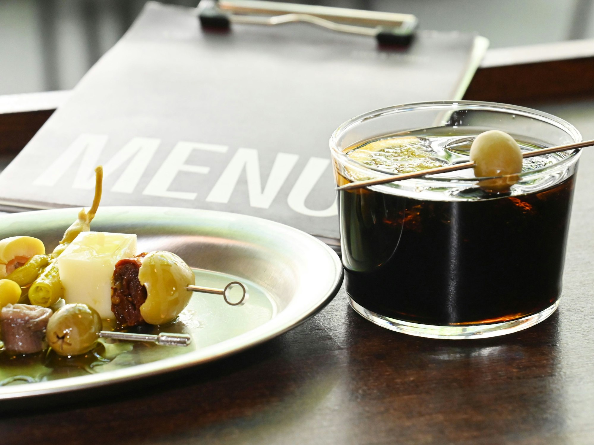 Ein Snack-Teller mit Spießchen und ein Cocktail mit Olive sind zu sehen.