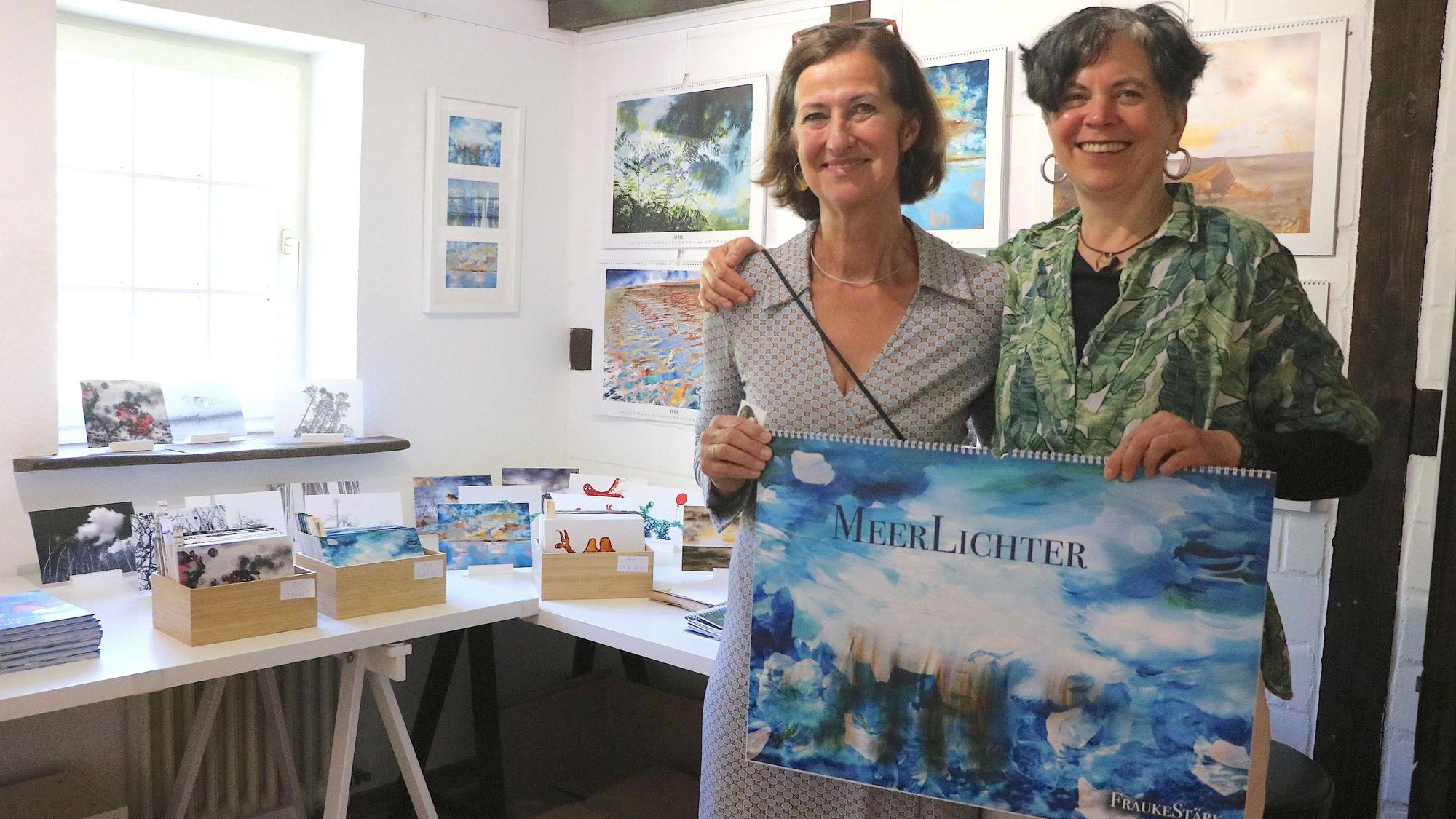 Zwei Frauen stehen nebeneinander, sie halten einen blauen Wandkalender in den Händen.