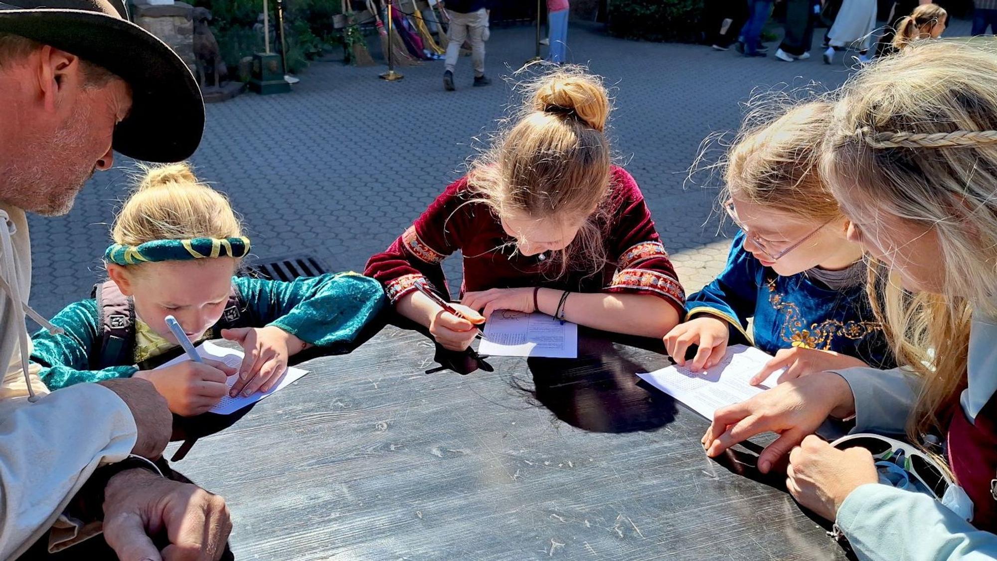 Die Familie sitzt rund um einen Tisch. Die Kinder füllen Fragebogen aus.